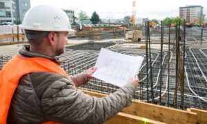 Infrastructure project manager in safety vest reviewing blueprints at a construction site in Grand Rapids