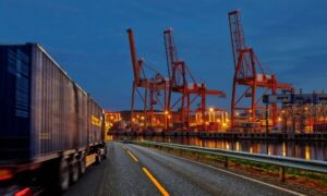 Transportation engineers design safe port access roads with freight trucks and shipping cranes in the background at dusk