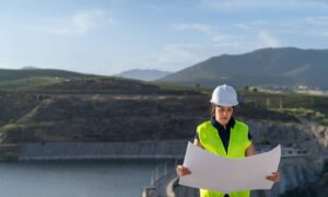 Civil engineer wearing a hard hat and safety vest reviewing blueprints during a dam inspection at a hydroelectric structure