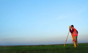 A construction engineer performing GPS surveying in an open field under clear skies, demonstrating precision and accuracy in modern construction engineering