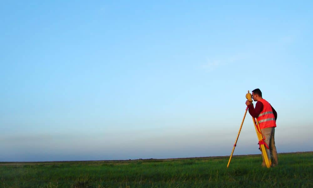 A construction engineer performing GPS surveying in an open field under clear skies, demonstrating precision and accuracy in modern construction engineering