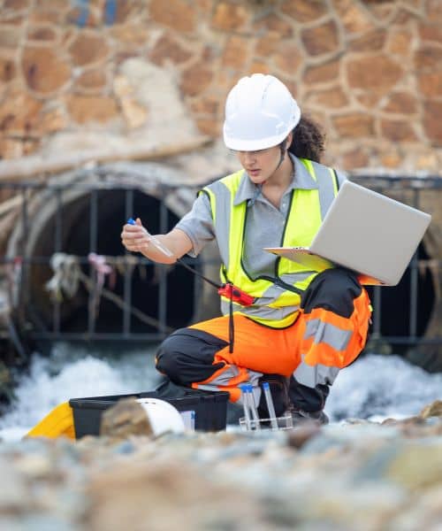 Civil engineer testing water flow and monitoring drainage design for stormwater management near an urban outflow