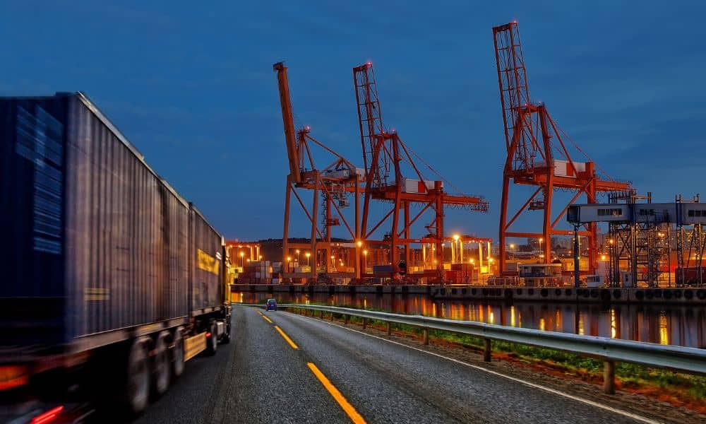 Transportation engineers design safe port access roads with freight trucks and shipping cranes in the background at dusk
