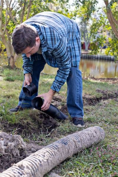 Homeowner fixing yard drainage pipe grading plan - ALTA SURVEY Michigan Homeowner repairing a yard drainage pipe as part of maintaining a proper grading plan for stormwater control
