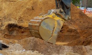 Excavator digging into soil during a stormwater design site inspection to check ground conditions