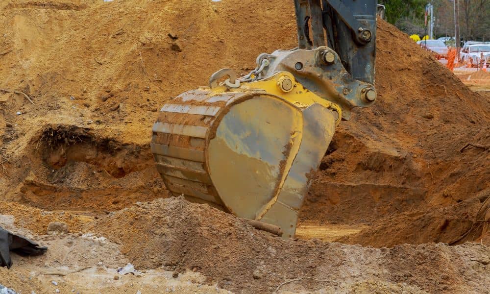 Excavator digging into soil during a stormwater design site inspection to check ground conditions